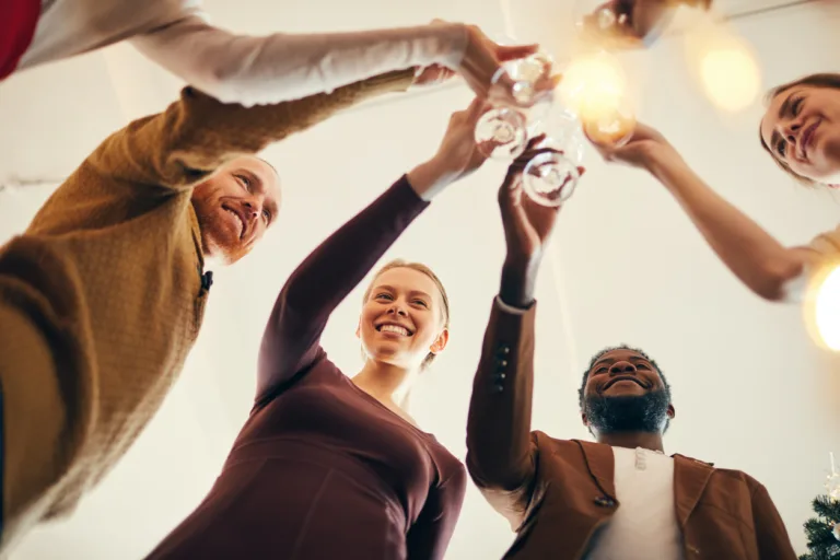 Low angle view at multi-ethnic group of people e clinking champagne glasses during Christmas party, copy space