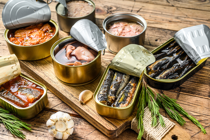 Various canned fish and seafood in a metal cans. Wooden background. Top view.
