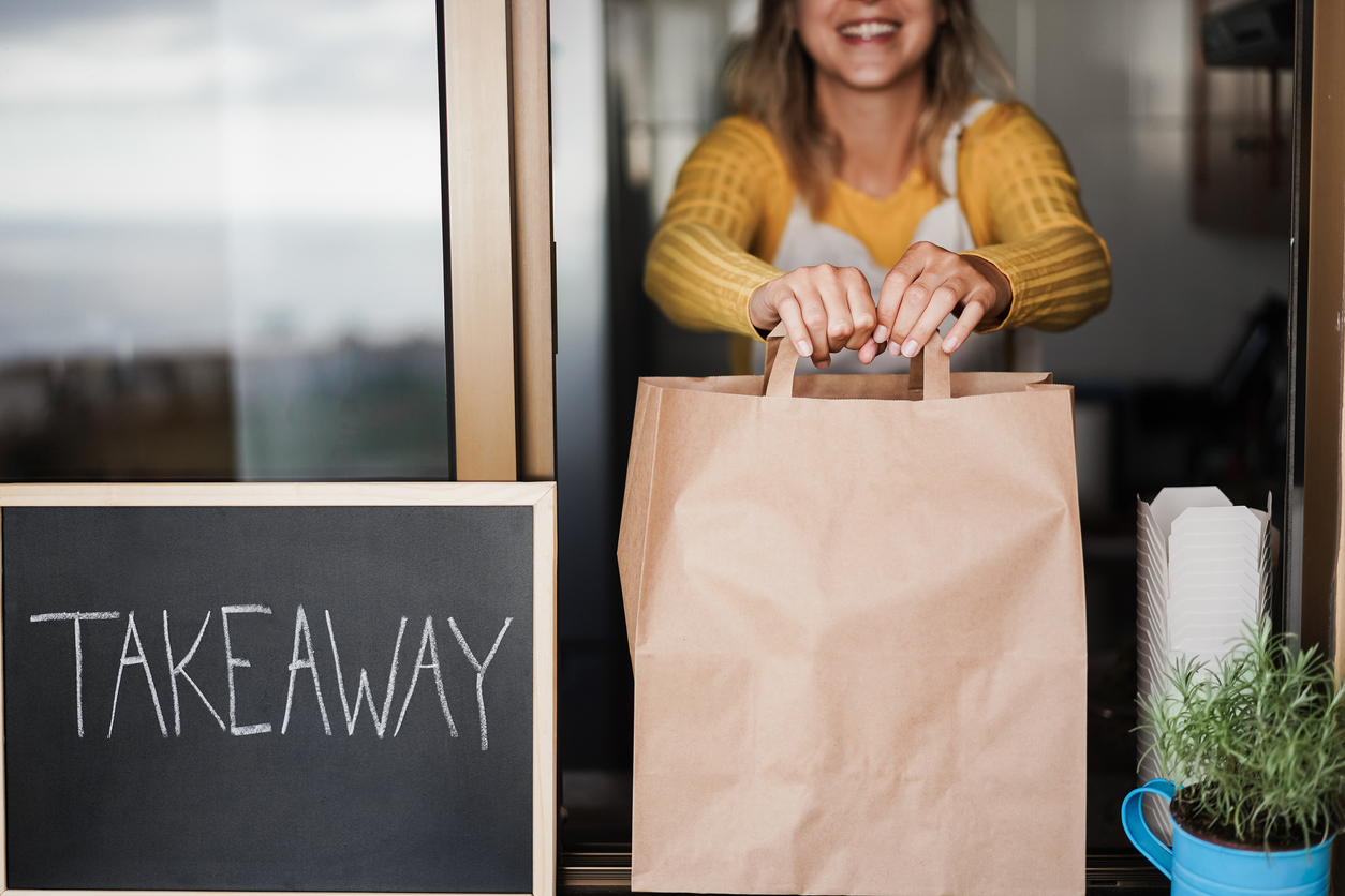 Young woman preparing takeaway food for fast delivery inside ghost kitchen - Focus on hands holding bag. ghost kitchen