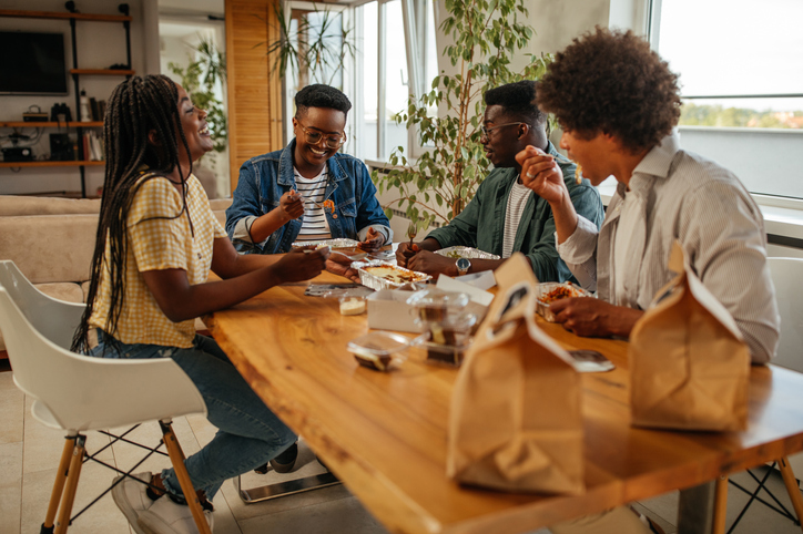 Group of friends eating a take-away food while sitting at the dining table