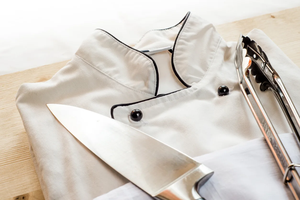 A chef coat and a knife on a wood board.