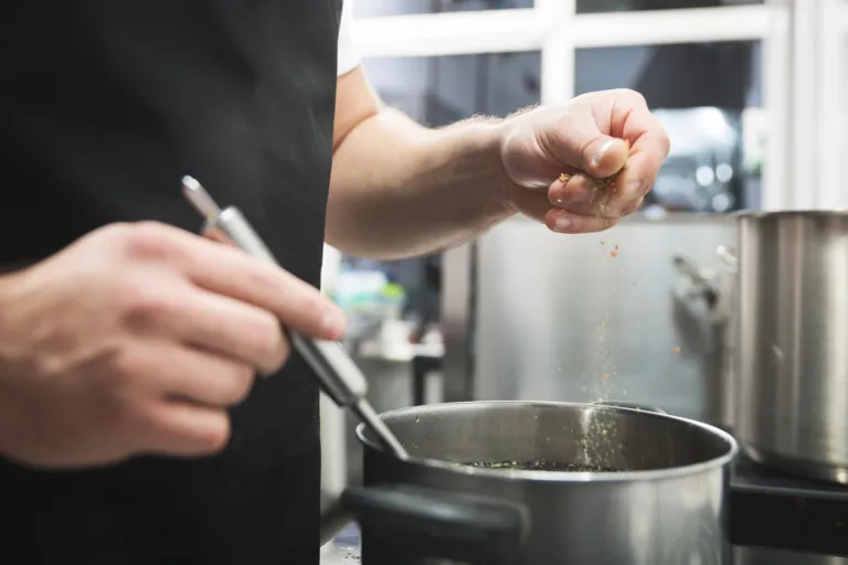 Closeup on chef hands pouring spices to the soup