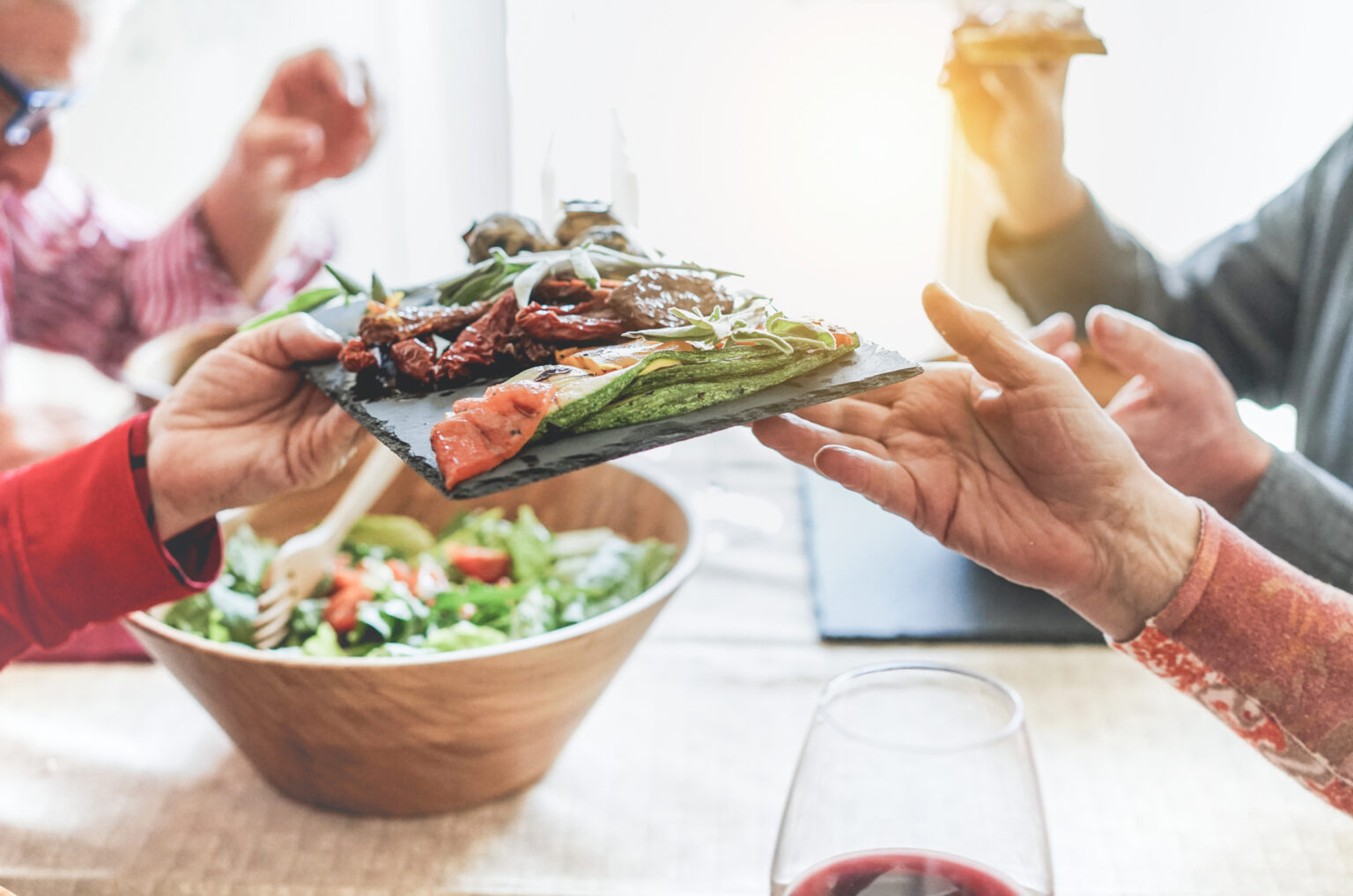 affordable dining options. Senior people having italian vegan vegetarian lunch at home - Mature friends eating bbq vegetables,fresh salads and toasting red wine - Healthy concept - Focus on courgette bottom dish - Warm filter