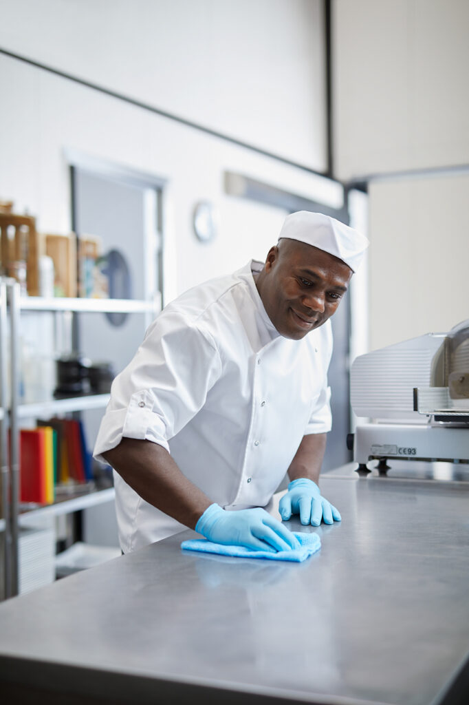 A male chef wipes down commercial kitchen countertops using a cloth and Diversey products.