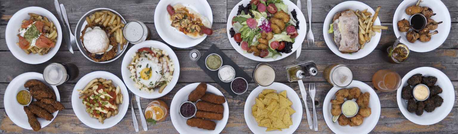 Gastronomy. Top view of the wooden table presenting lots of gourmet fast food dishes such as fried shrimps, mozzarella sticks, fried chicken sticks, nachos, hot dog, shrimps salad, fries and spinach fritters. All from foodservice suppliers