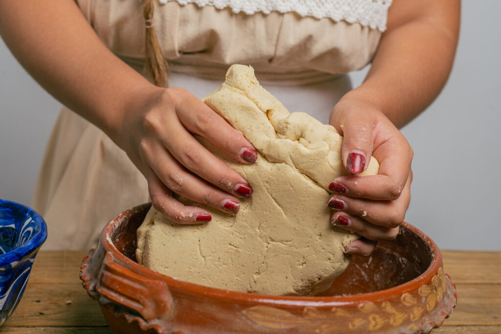 Person doughing nixtamalized corn dough in a clay bowl. Typical Mexican food. Global ingredient sourcing