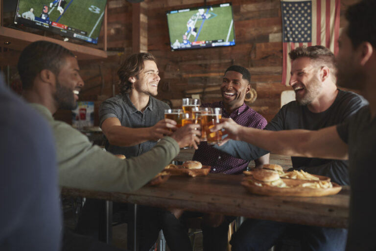 Male Friends Drinking Beer And Eating Burgers In Sports Bar