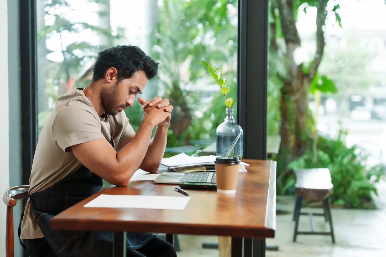 Businessman of coffee shop, small business, multiethnic man working with laptop, contemplating accounting documents And there was disposable brown paper coffee cup. The shop is minimalist.