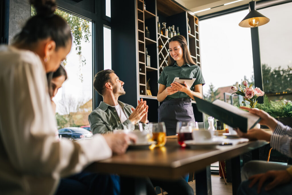 Group of people ordering food from the waitress. Waitress writing orders down on tablet. Undecided people reading the menu while the waitress waits and helps them.