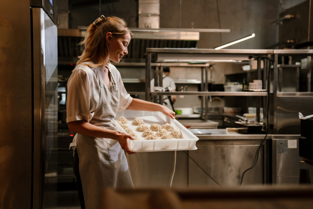 Young white woman cook wearing apron preparing meals for a restaurant in kitchen