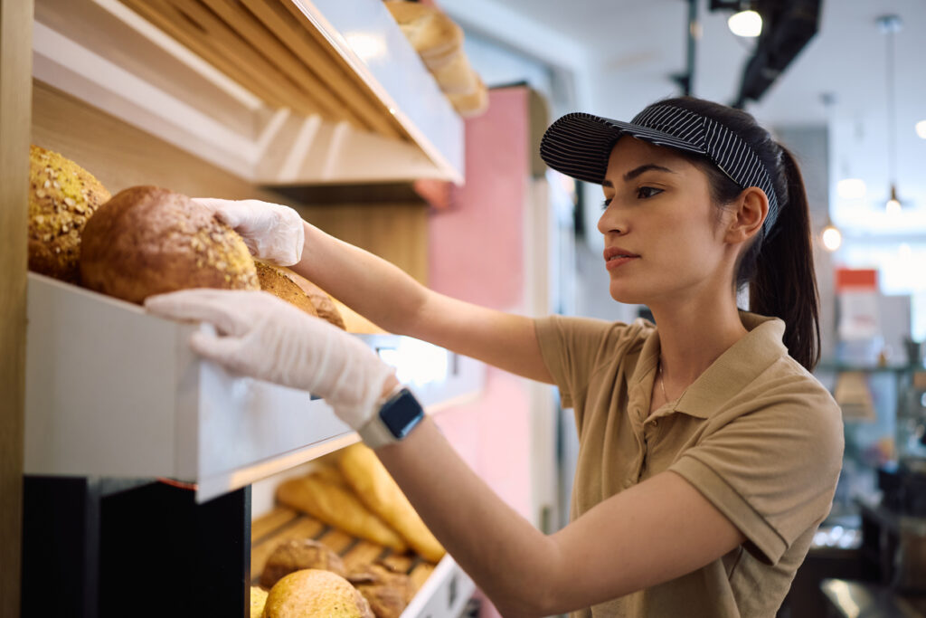 Female baker arranging fresh bread on shelves in a bakery.