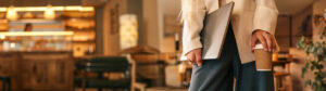 A woman in a blazer stands in a cafe, holding a laptop and a coffee cup. The background is blurred, creating a modern and minimal aesthetic. restaurant industry leadership advice
