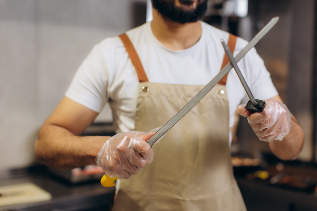 Cook in apron and gloves sharpening a professional knife with a steel, ensuring sharp blades for food preparation
