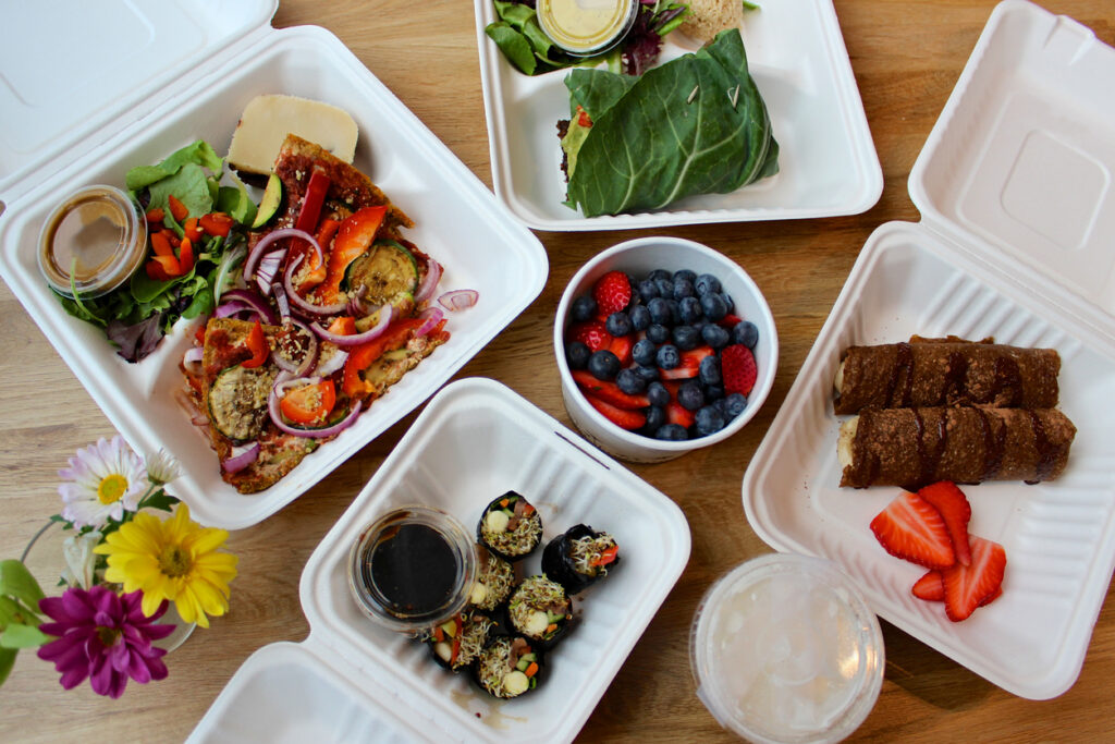A day's worth of meals from a raw-vegan delivery service, ready for a cleanse or detox. Includes: crepes, berries, collard green wraps, sushi, salad and pizza.