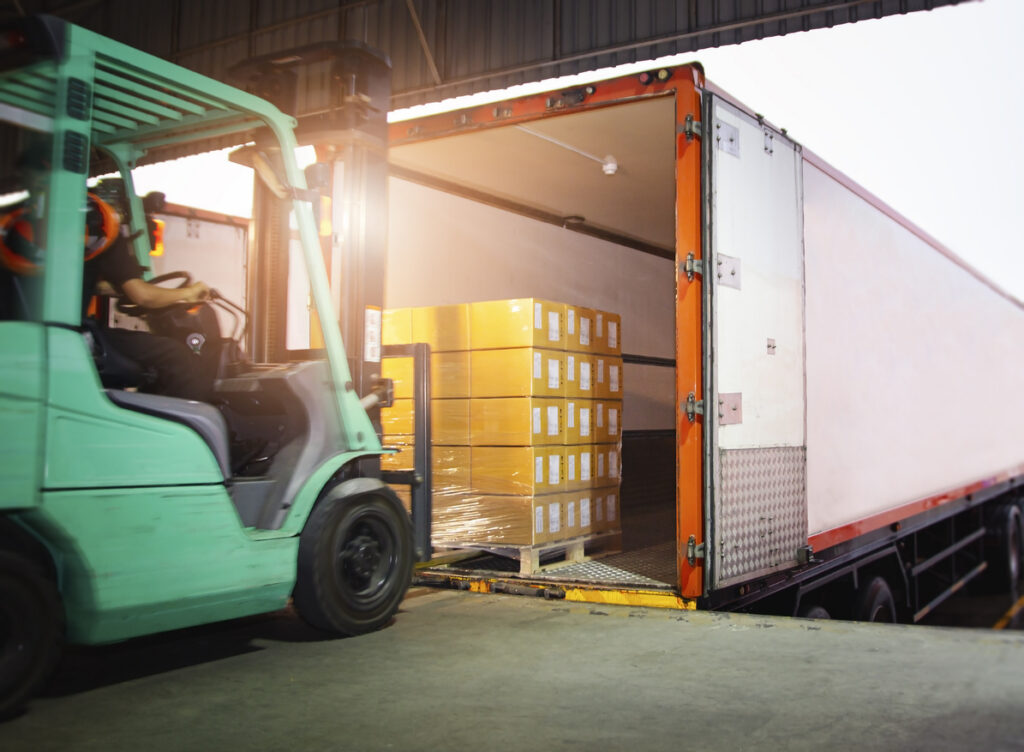 Forklift Driver Loading Package Boxes into Cargo Container. Cargo Trailer Truck Parked Loading at Dock Warehouse. Shipment Delivery Service. Shipping Warehouse Logistics. Freight Truck Transportation.